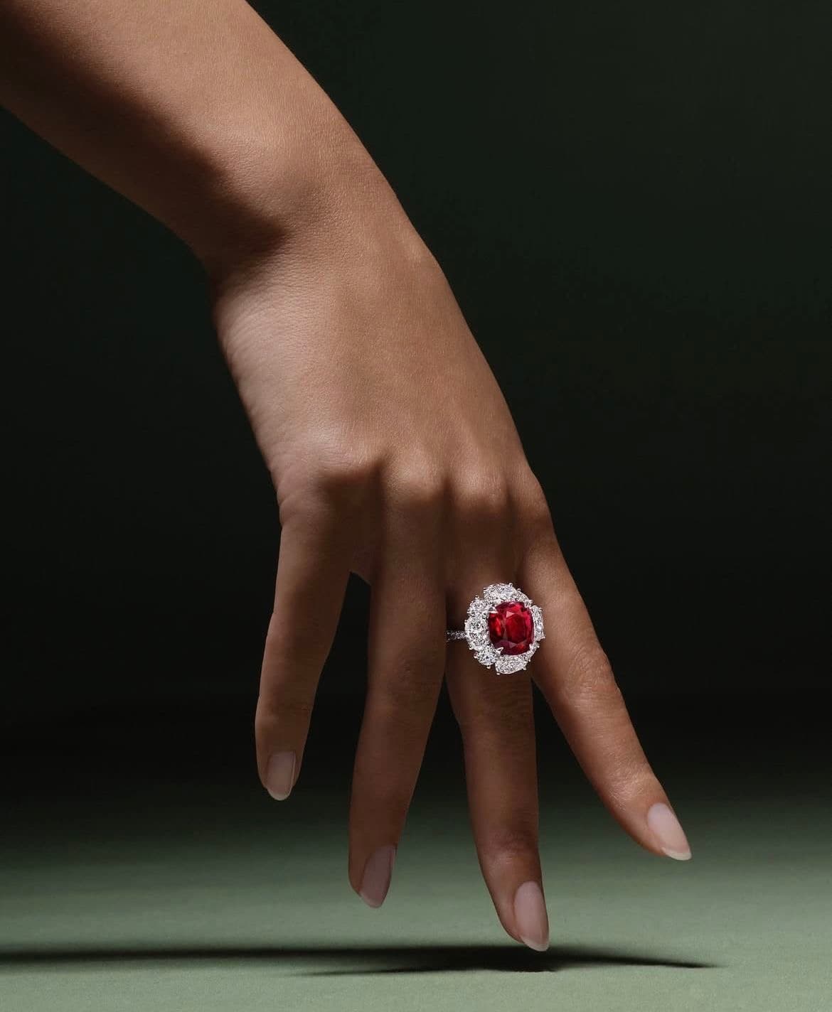 A hand wearing a ring: a red stone surrounded by diamonds